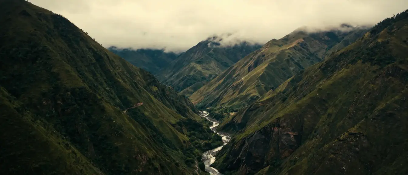 A green Andean valley under low cloud, a river at its floor